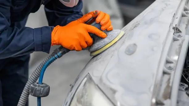 A man with an orange glove carefully polishes a car, ensuring it looks pristine and well-maintained, just like our Bumper Repair Houston Texas services keep your vehicle in top conditio