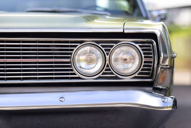 Detailed close up of a classic car's front grille and polish chrome bumper highlighting its unique features and timeless elegance