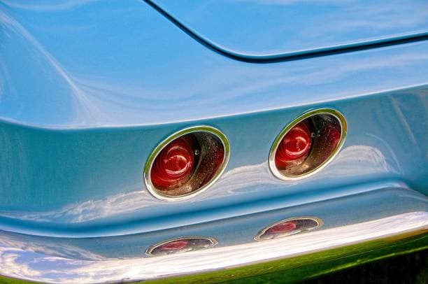 The tail lights of a blue Corvette highlighting their modern design and bright red glow against the polish chrome bumper and car's exterior