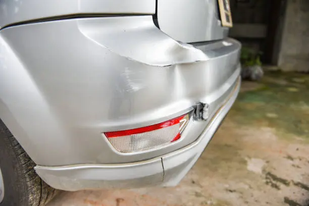 A silver vehicle with a dented rear bumper and a cracked taillight, showcasing the steel bumper dent repair cost for fixing the damage