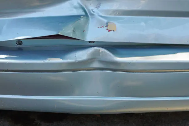 Close-up of a car rear bumper with visible dents and damage, highlighting the steel bumper dent repair cost for restoration