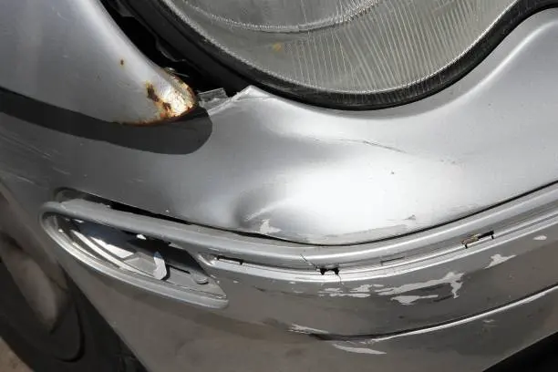 Silver car with a dented bumper and rust near the headlight, highlighting the steel bumper dent repair cost for restoration