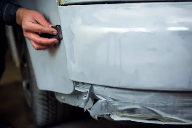 Who can fix my bumper Close-up of a hand working on a car bumper with a gray surface coat at Westside Collisio