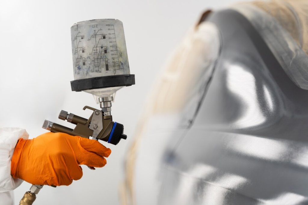 A person wearing an orange glove sprays a car with cleaning solution, ensuring a thorough wash and shine while considering the bumper repair and paint cost for a complete finish