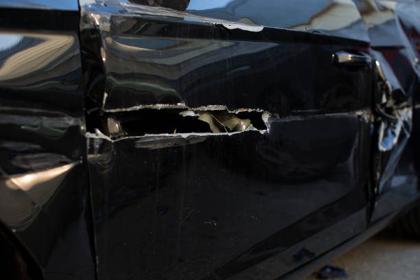 A black vehicle with a shattered window and a prominent dent reflecting signs of wear or possible vandalism requiring car bumper hole repair