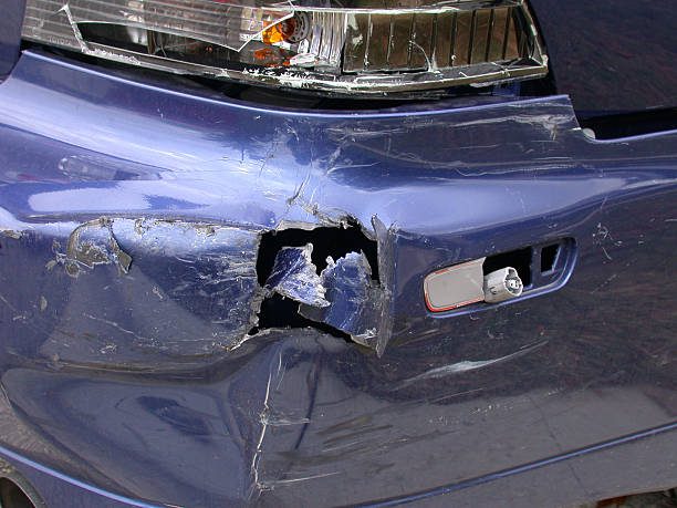 A blue car exhibiting damage with noticeable dents and scratches positioned on a street needing car bumper hole repair