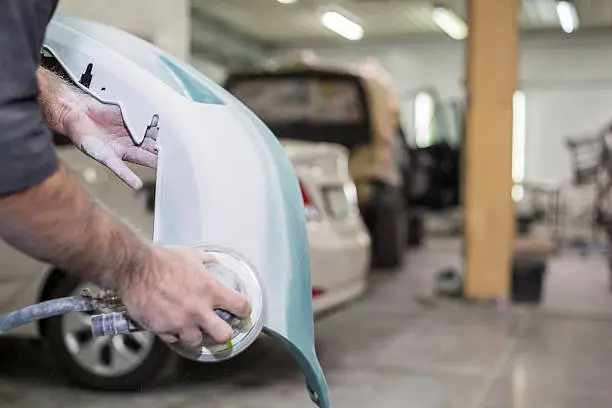 A person inspects the front of a damaged car their hand resting on the surface reflecting concern over the vehicle's state and the bumper repair cost