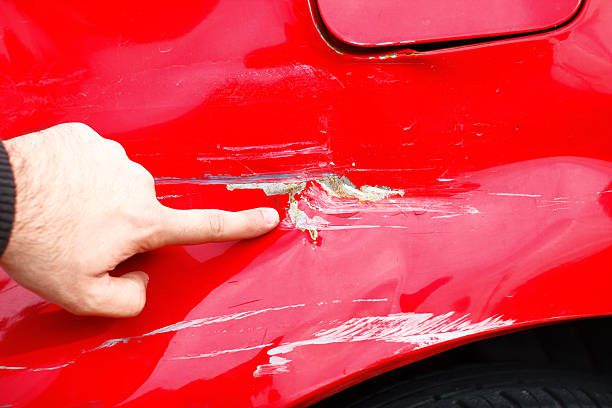 A person is interacting with a red car which displays a significant dent on its body highlighting the need to remove bumper scuffs