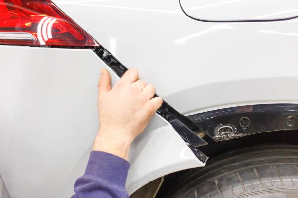 A person is repairing a car's bumper focused on how to put a bumper on a car to restore its appearance and functionality