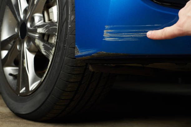 A person is seen touching the front of a blue car emphasizing the tactile engagement with the automobile and the potential need to remove bumper scuffs