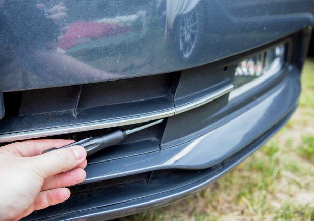 A person skillfully uses a screwdriver to detach the front bumper demonstrating how to put a bumper on a car with effective automotive repair techniques