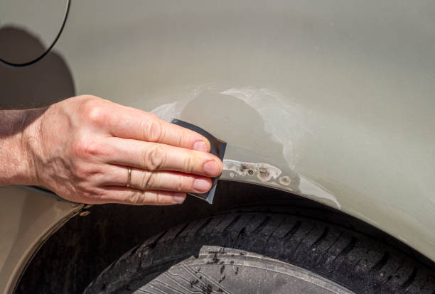 A person using a specialized tool to effectively remove a dent from a car's surface demonstrating the importance of small bumper crack repair